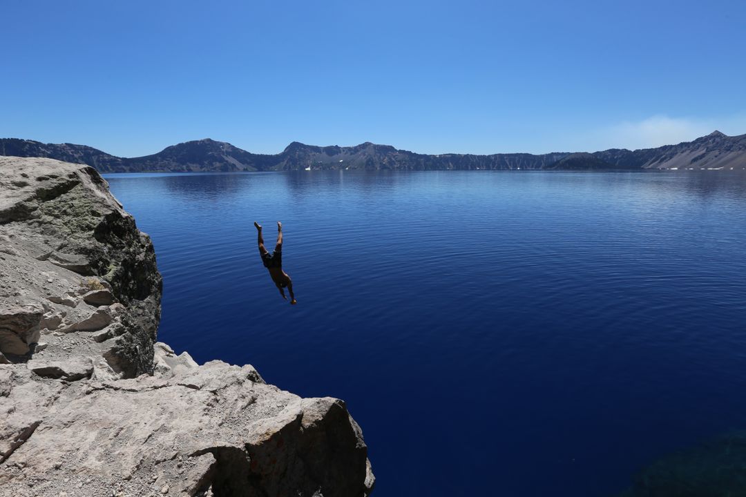 Daring Cliff Dive into Serene Blue Lake with Mountain View