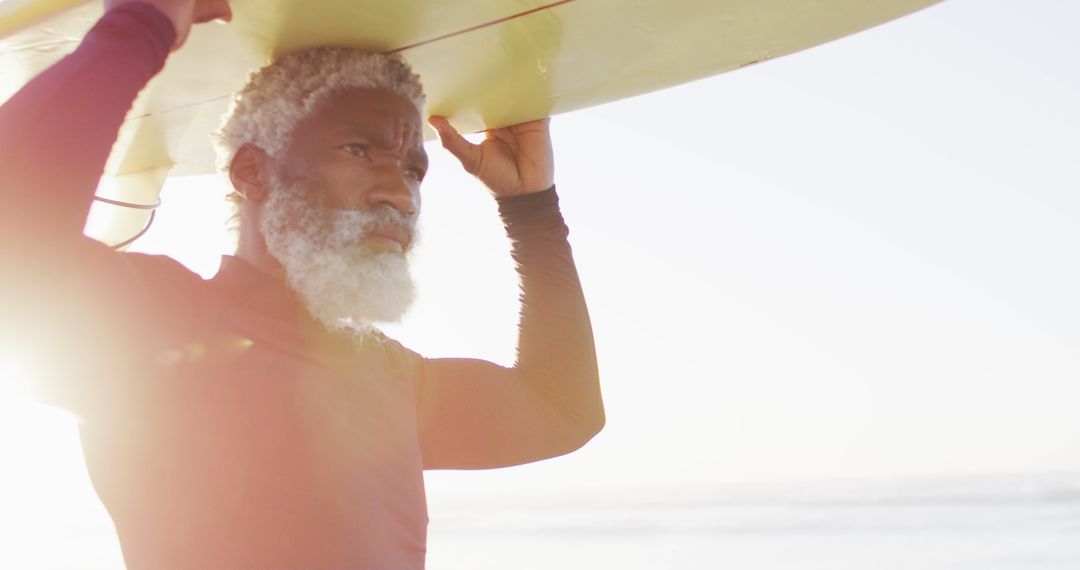 Elderly surfer carrying board on beach at sunset - Free Images, Stock Photos and Pictures on Pikwizard.com