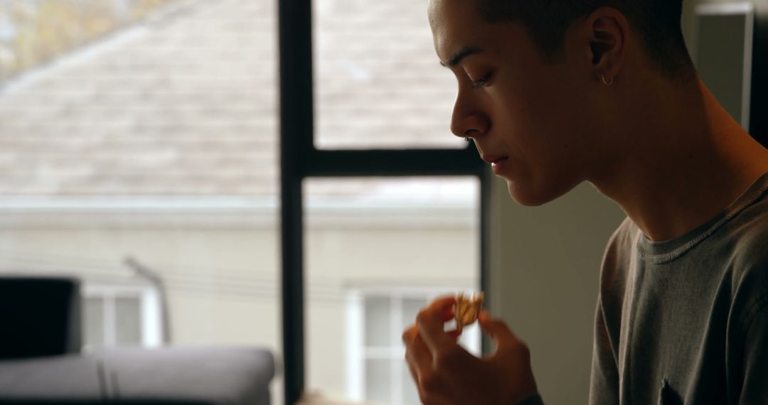 Pensive Young Man Enjoying Snack by Window in Cozy Room - Free Images, Stock Photos and Pictures on Pikwizard.com