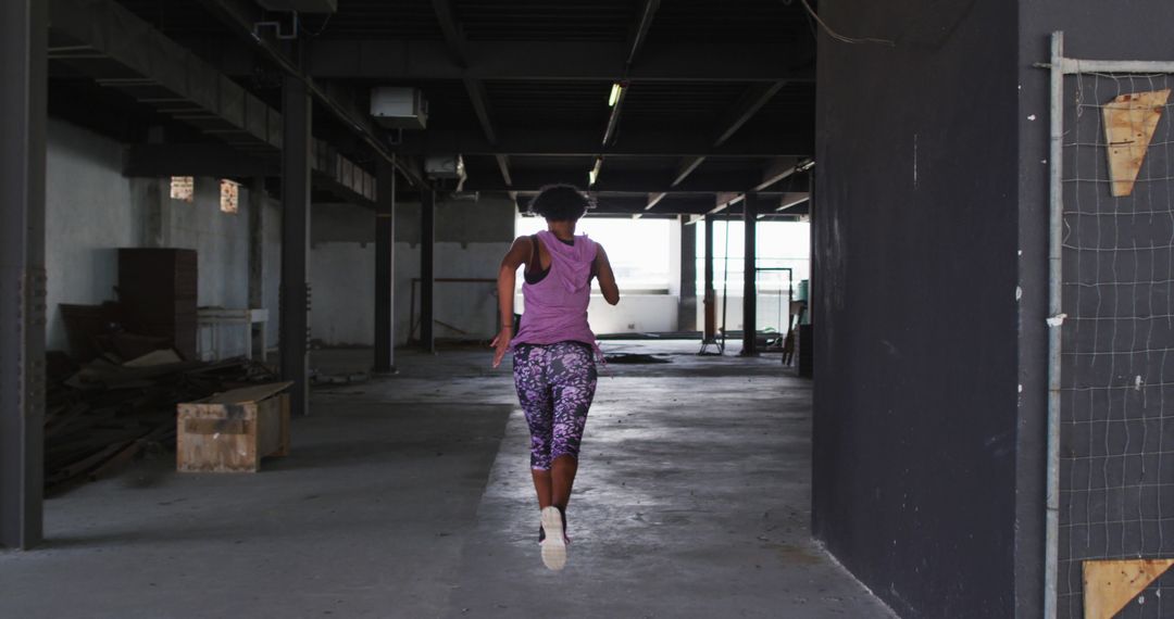 African american woman wearing sports clothing jogging through an empty urban building - Free Images, Stock Photos and Pictures on Pikwizard.com