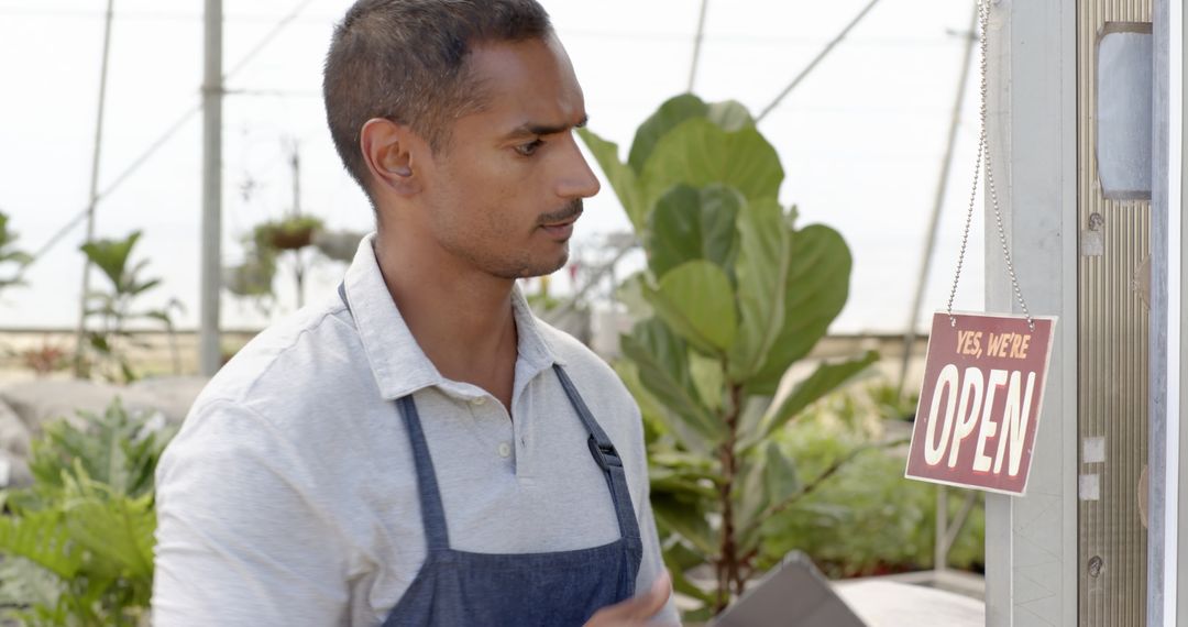 Male Nursery Owner Adjusting Open Sign in Greenhouse