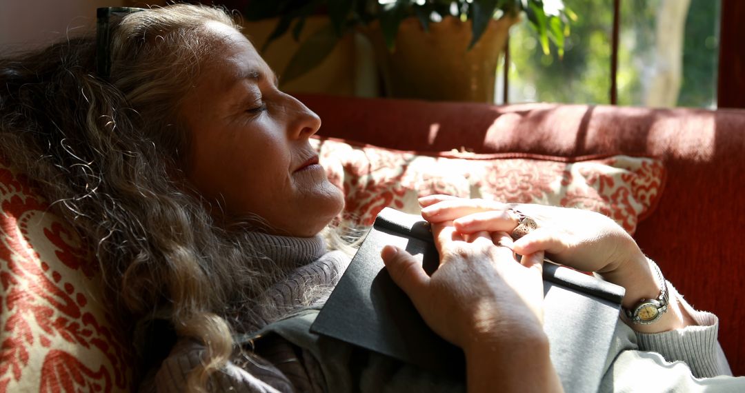 Senior Woman Relaxing on Couch Holding Book in Sunlit Room - Free Images, Stock Photos and Pictures on Pikwizard.com