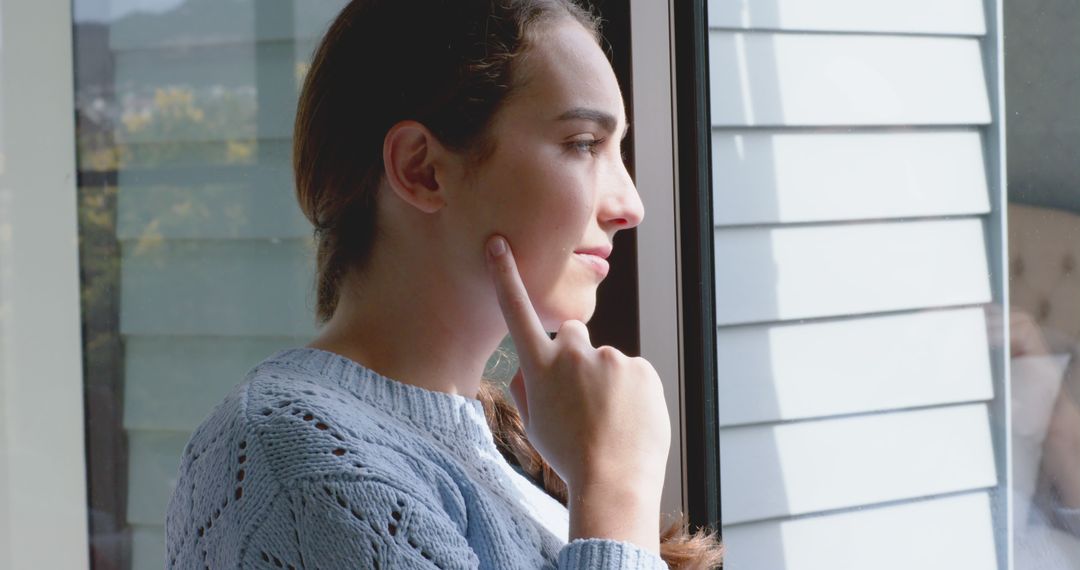 Pensive Woman Looking Out Window in Cozy Sweater - Free Images, Stock Photos and Pictures on Pikwizard.com