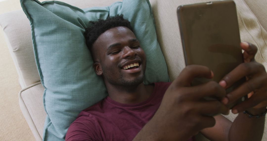 Laughing man using tablet while lying on couch at home - Free Images, Stock Photos and Pictures on Pikwizard.com