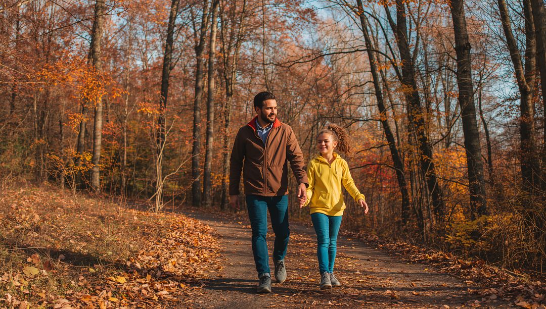 Walking father and daughter holding hands on autumn forest trail, smiling and bonding
