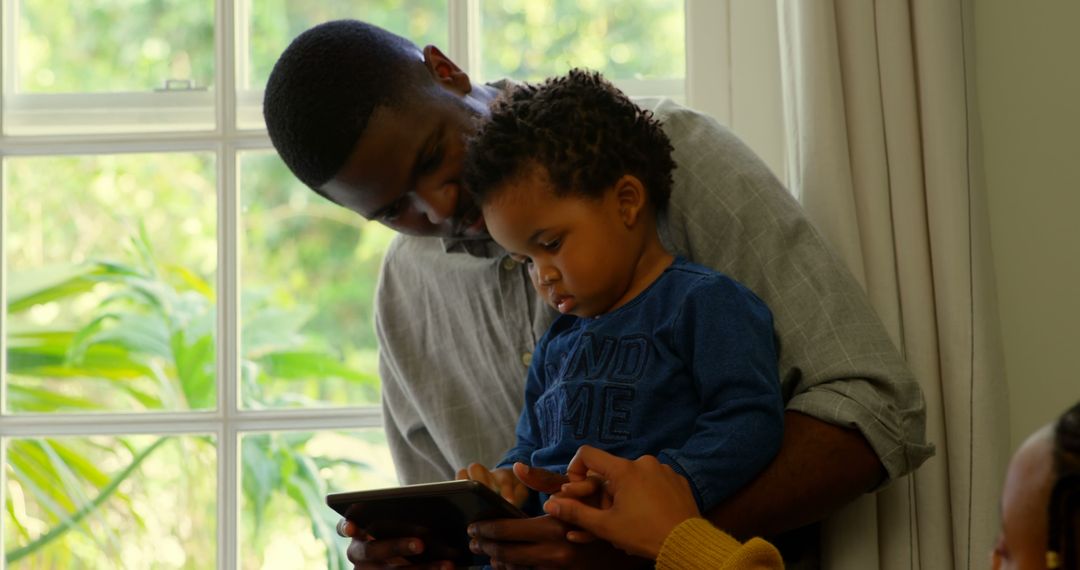 Father and Child Using Digital Tablet by Window in Bright Living Room - Free Images, Stock Photos and Pictures on Pikwizard.com