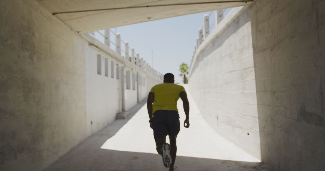 Athletic man running through urban tunnel in bright sunlight - Free Images, Stock Photos and Pictures on Pikwizard.com