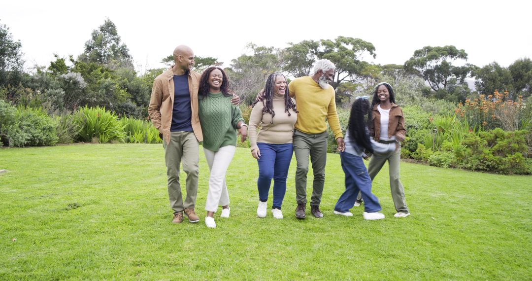 Multigenerational Black family walking together in lush green park, smiling and bonding