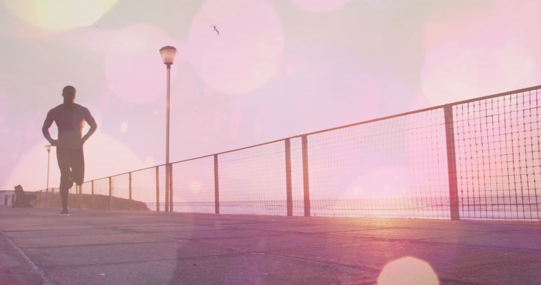 Silhouette of Man Running by Ocean at Sunset with Light Bokeh Effect