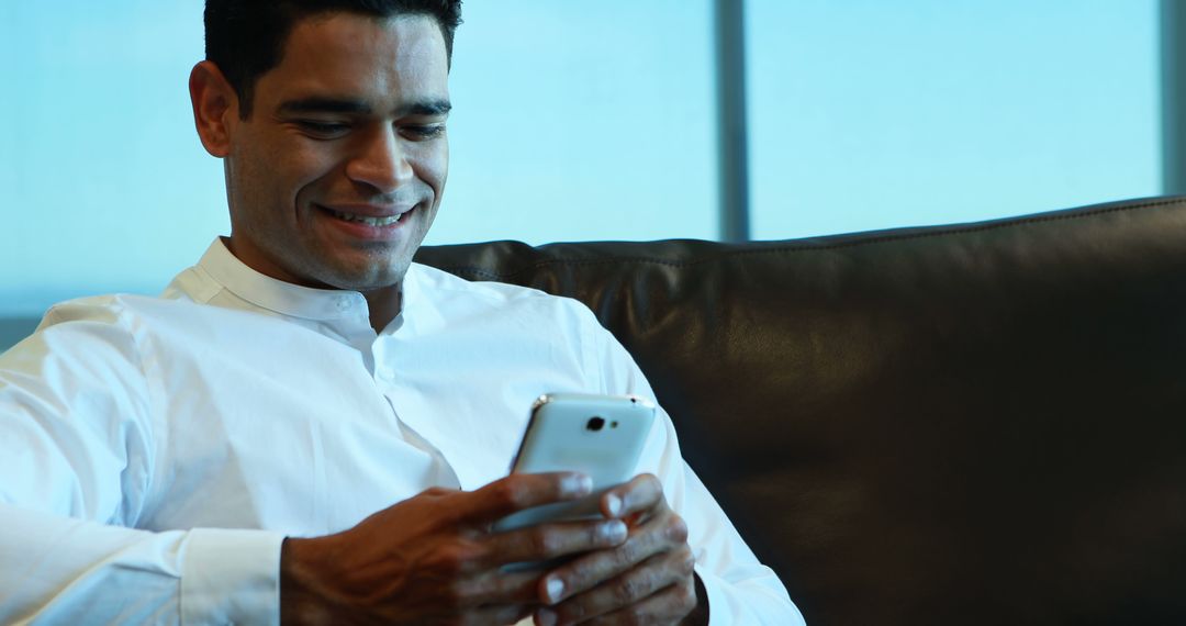 Man Smiling While Using Smartphone on Sofa - Free Images, Stock Photos and Pictures on Pikwizard.com