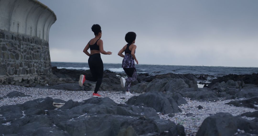 Two Women Running Along Rocky Beach - Free Images, Stock Photos and Pictures on Pikwizard.com