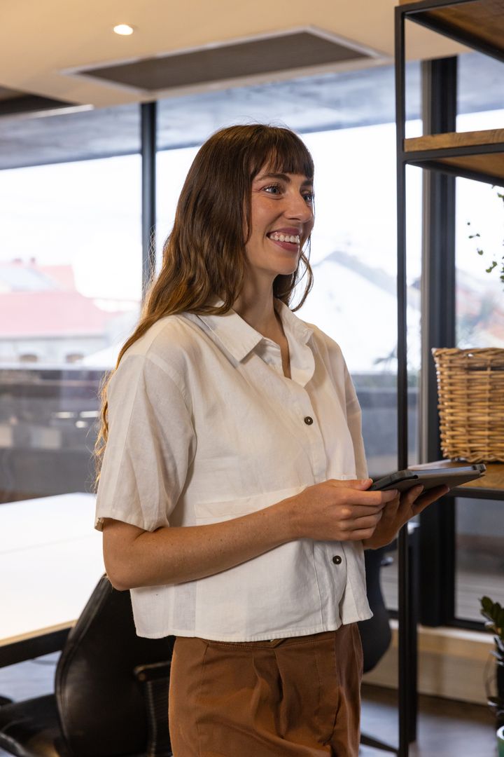 Smiling Professional Woman Holding Tablet in Modern Office Environment