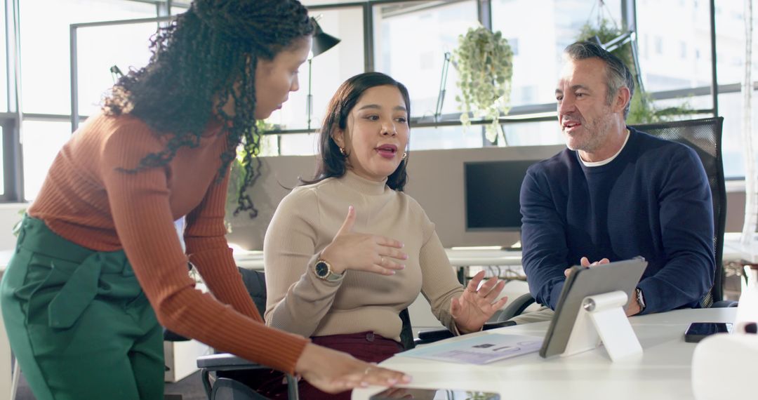 Multicultural team collaborating around tablet and charts in sunlit modern office meeting
