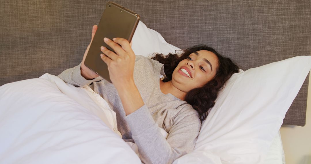 Young Woman Relaxing in Bed and Smiling While Using Tablet - Free Images, Stock Photos and Pictures on Pikwizard.com