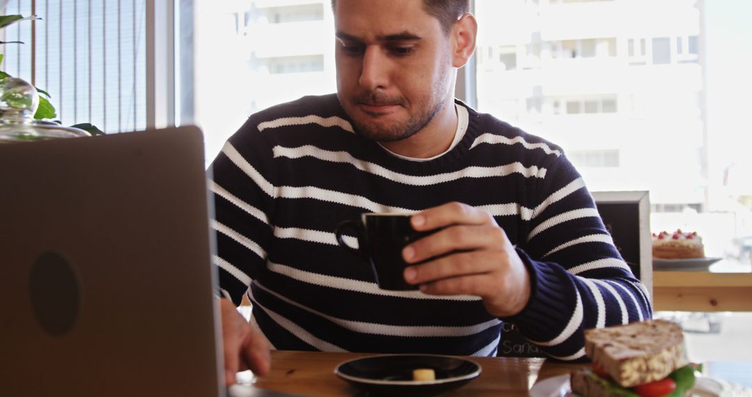 Young Man Enjoying Coffee While Using Laptop in Cafe