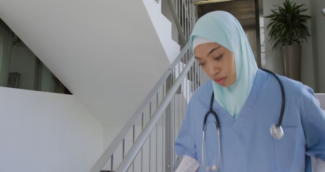 Female Muslim Nurse Walking Down Hospital Stairs in Scrubs - Free Images, Stock Photos and Pictures on Pikwizard.com