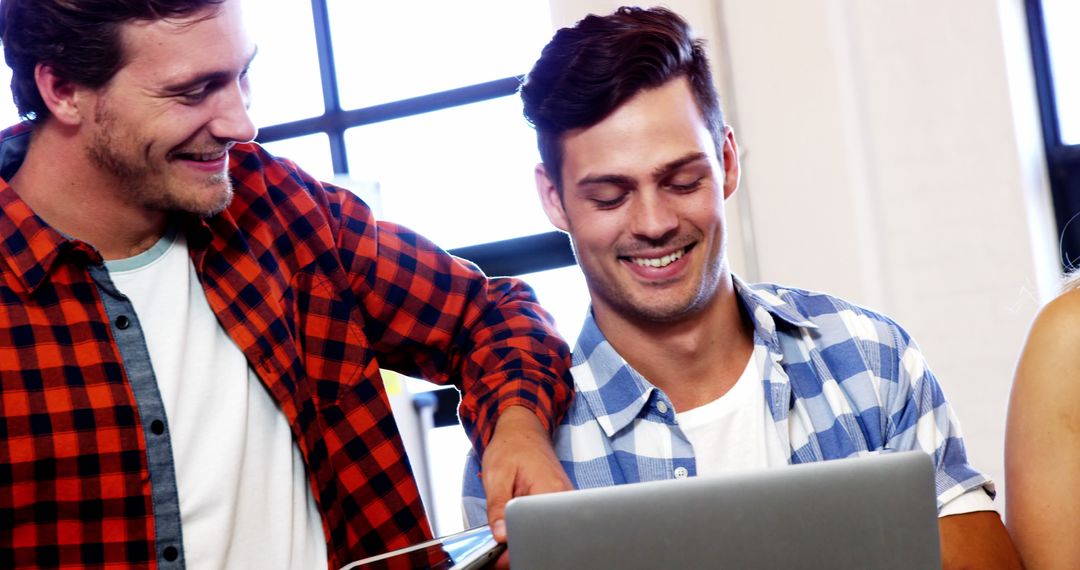 Young Men Collaborating Cheerfully on Laptop in Modern Office