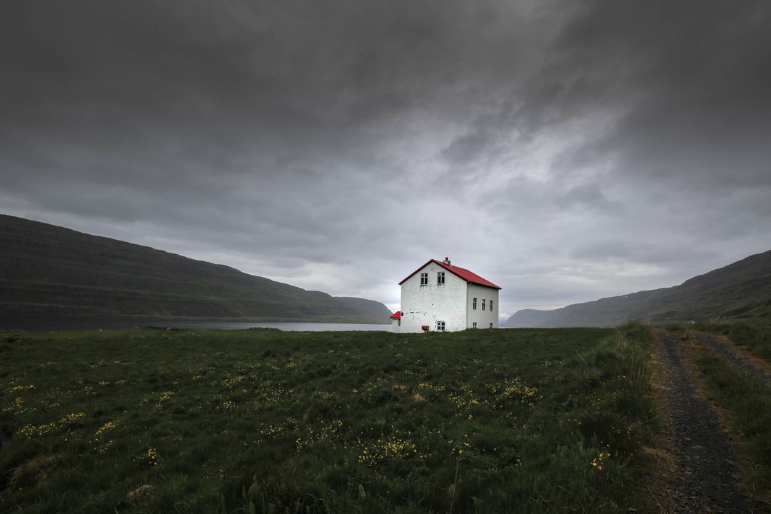 Solitary White House with Red Roof on Moody Fjord Meadow under Stormy Overcast Sky