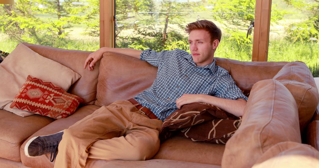 Young Man Relaxing on Couch in Bright Living Room - Free Images, Stock Photos and Pictures on Pikwizard.com