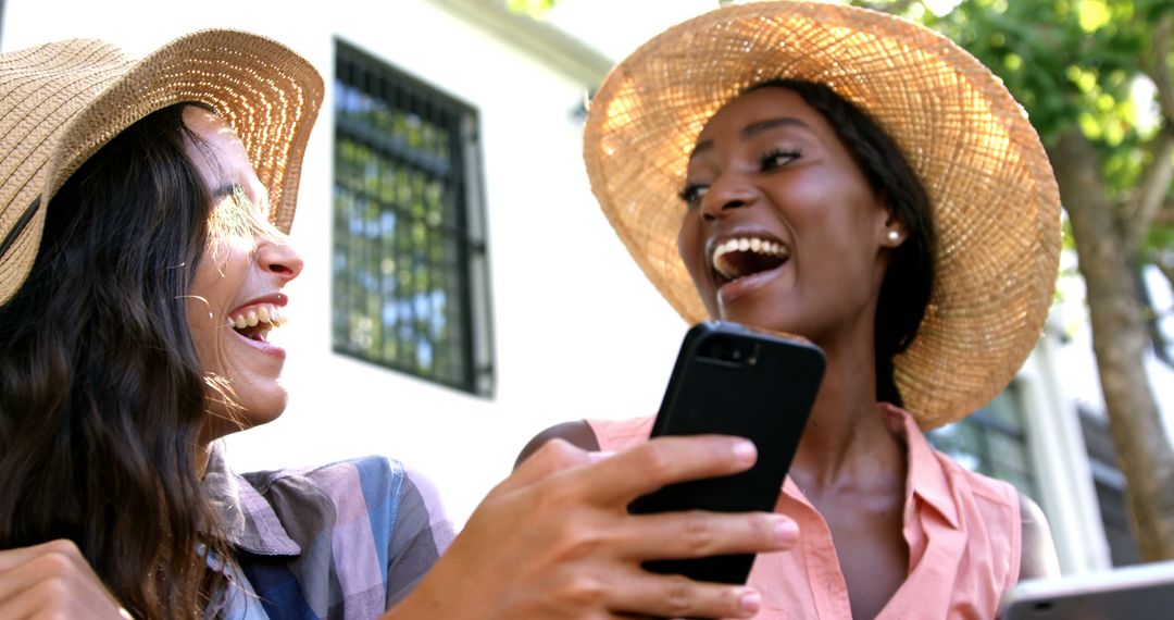 Happy Women Enjoying Summer Outdoors with Smartphones and Sun Hats - Free Images, Stock Photos and Pictures on Pikwizard.com