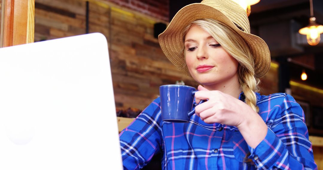 Blonde Woman Wearing Straw Hat Working on Laptop While Sipping Coffee - Free Images, Stock Photos and Pictures on Pikwizard.com