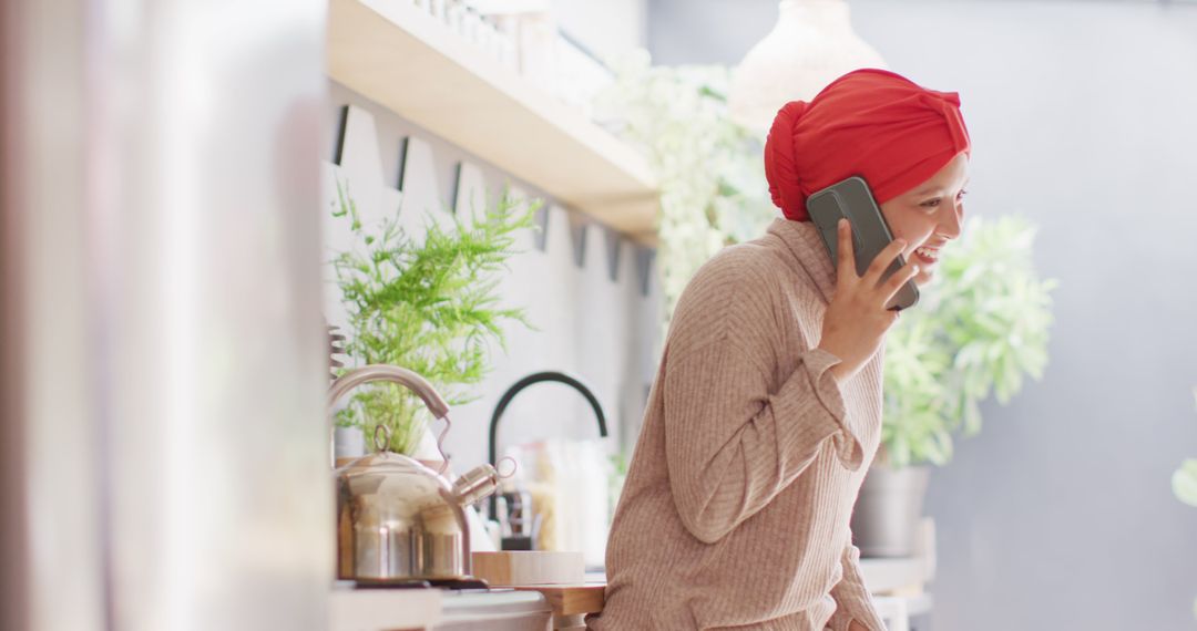 Image of laughing biracial woman in hijab talking on smartphone standing in kitchen at home - Free Images, Stock Photos and Pictures on Pikwizard.com