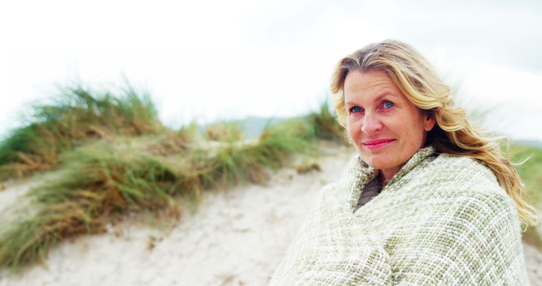 Smiling Mature Woman Wrapped in Blanket on Sandy Beach - Free Images, Stock Photos and Pictures on Pikwizard.com