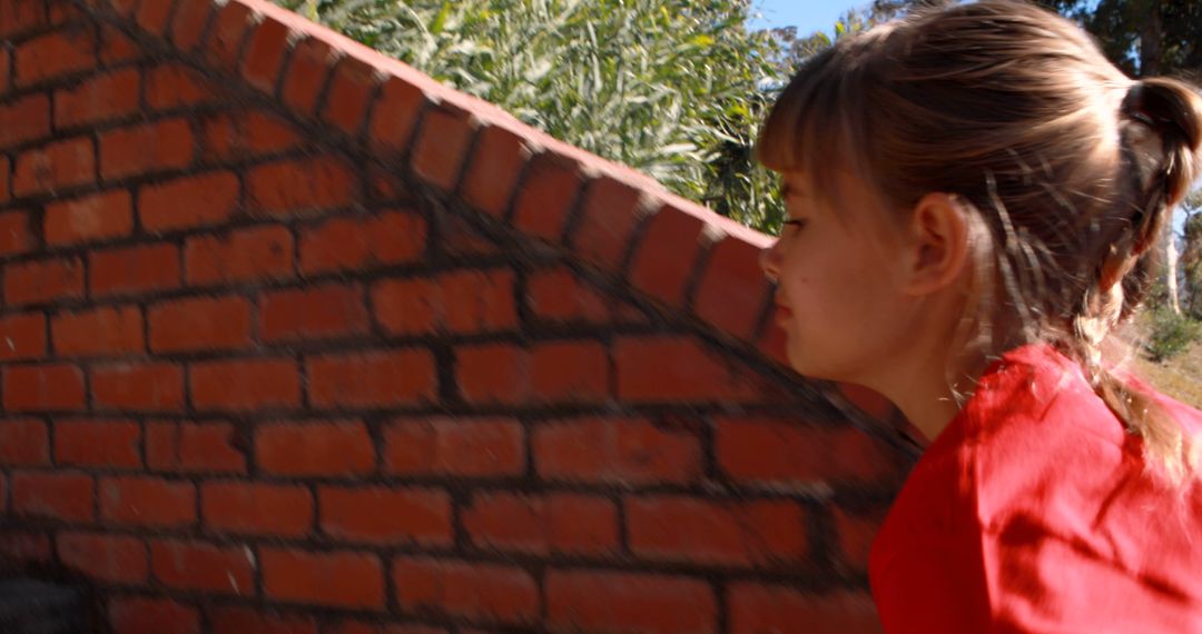 Young Girl Playing Hide and Seek Behind Brick Wall in Sunny Park - Free Images, Stock Photos and Pictures on Pikwizard.com