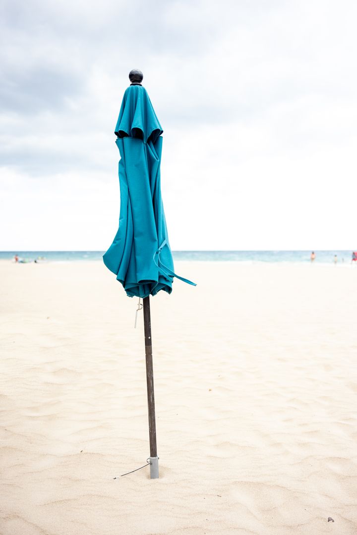 Folded Turquoise Beach Umbrella Standing on Empty Sandy Beach with Ocean Horizon