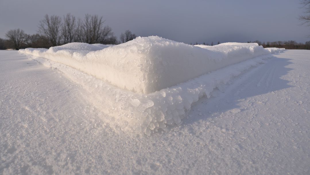 Triangular layered snow and ice ridge casting soft shadows across rural winter field