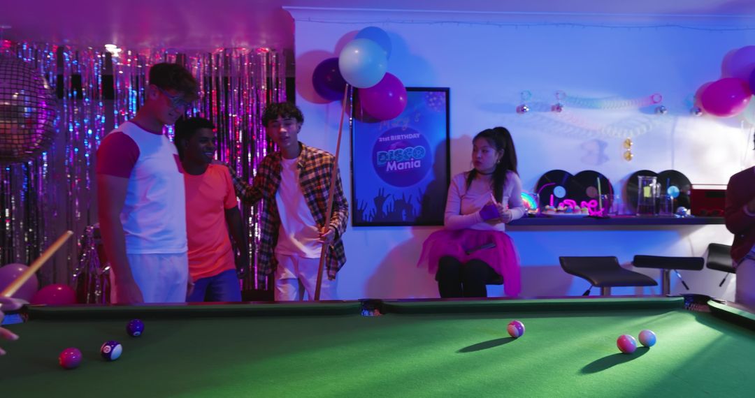 Multicultural friends playing pool at neon disco party with balloons, tinsel and cues