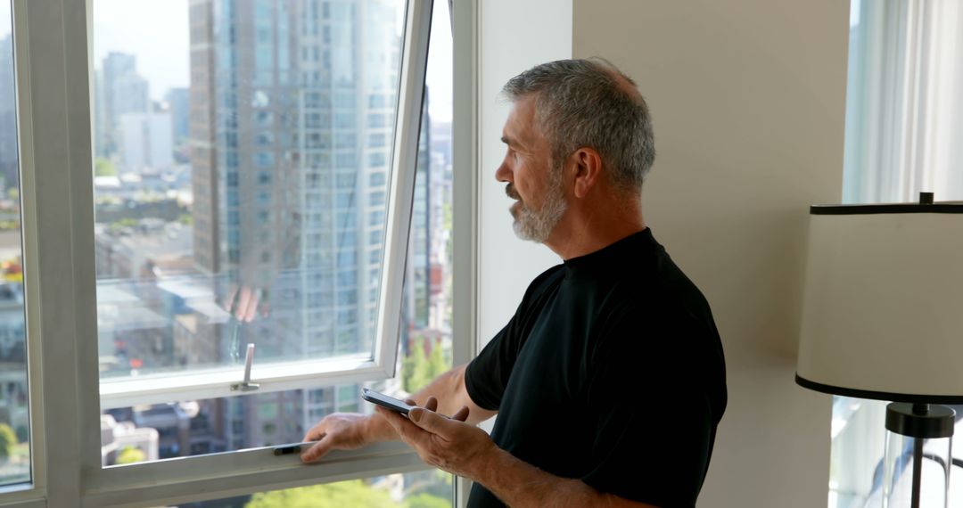 Bearded Man Using Smart Home Device by Window in Modern Apartment - Free Images, Stock Photos and Pictures on Pikwizard.com