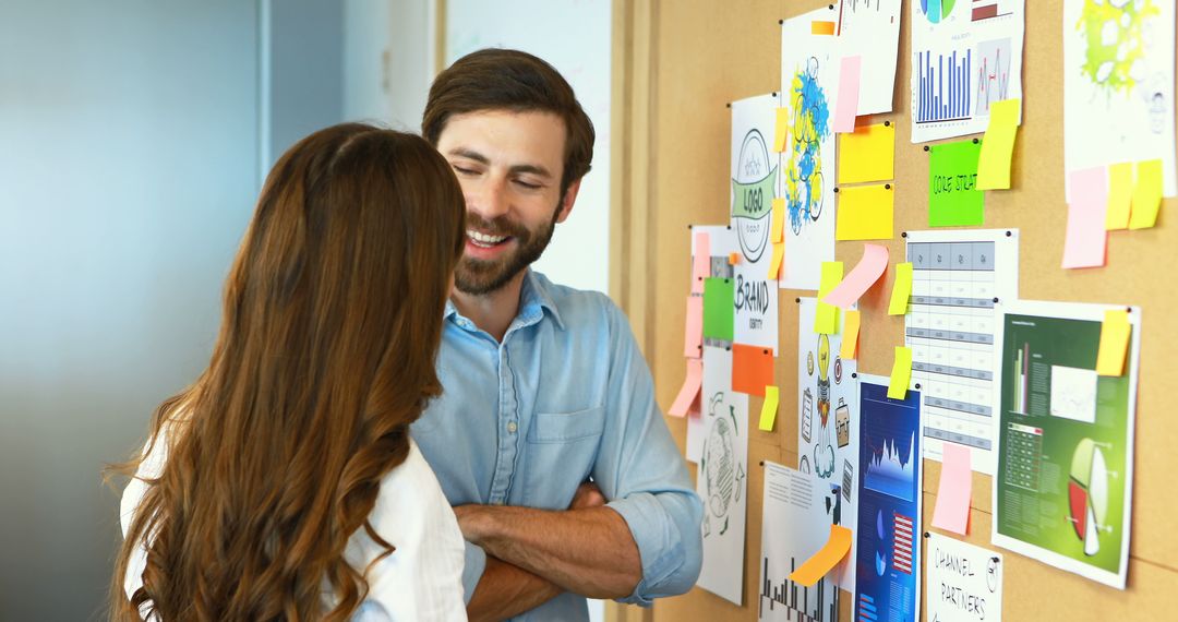 Smiling coworkers discussing project ideas on cork board in creative office - Free Images, Stock Photos and Pictures on Pikwizard.com