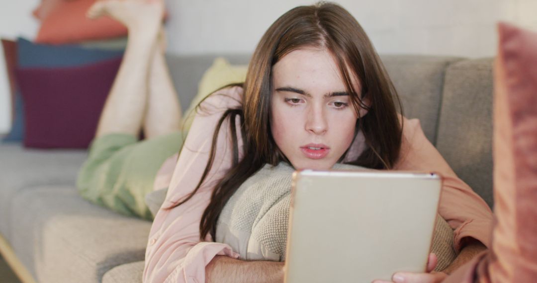 Caucasian non-binary transgender woman lying on sofa, using tablet - Free Images, Stock Photos and Pictures on Pikwizard.com