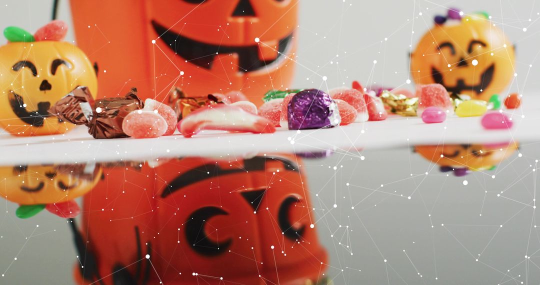 Halloween candy reflecting on glossy surface with jack-o-lantern buckets and sweets