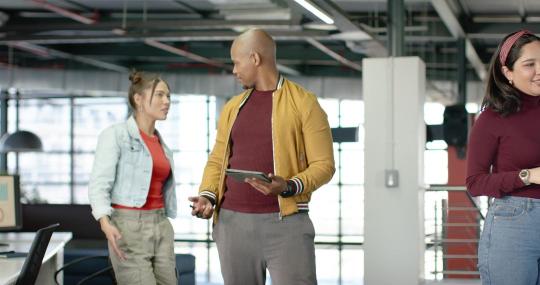 Diverse team discussing project in open-plan office using tablet and casual attire