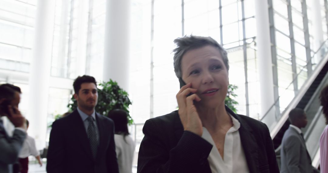 Businesswoman talking on cellphone in busy office lobby - Free Images, Stock Photos and Pictures on Pikwizard.com