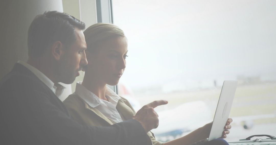 Business partners collaborating over laptop at airport gate with runway and airplane view