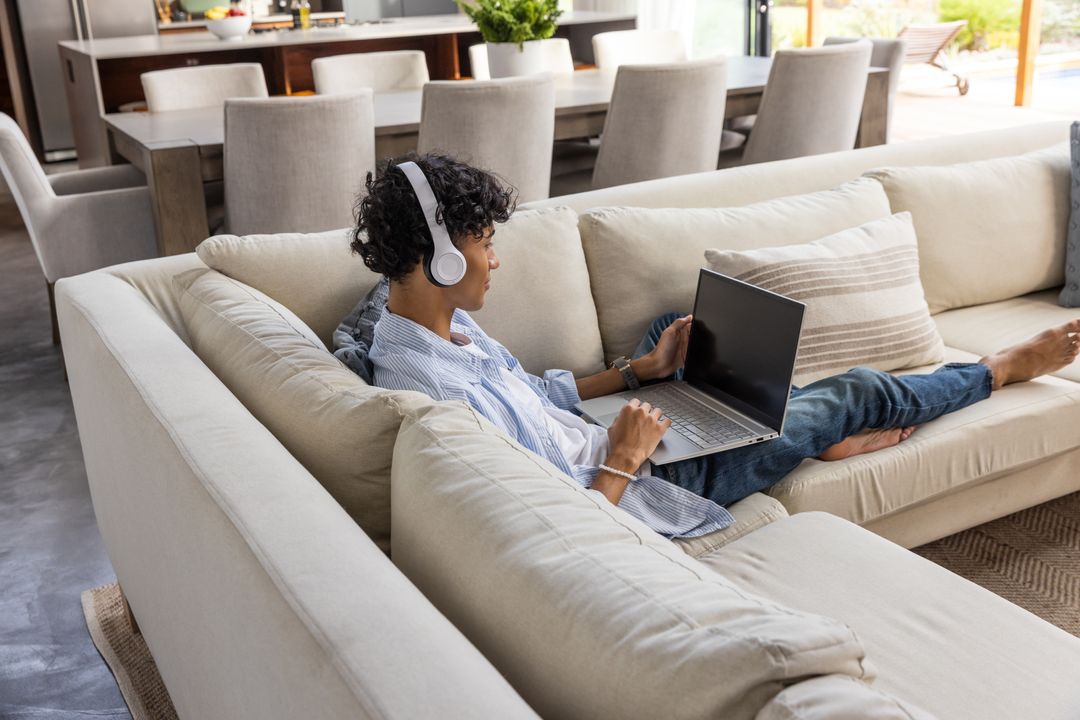 Relaxed Man Using Laptop on Sofa with Headphones in Modern Home