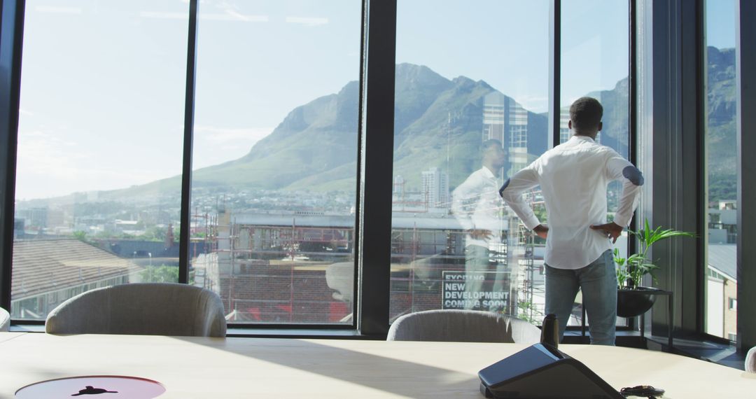 Businessman Overlooking City from High-Rise Office with Scenic Mountain View - Free Images, Stock Photos and Pictures on Pikwizard.com