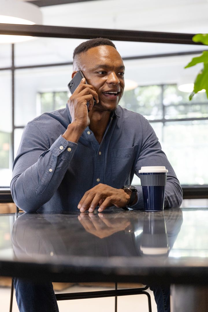Confident Professional Talking on Smartphone with Coffee in Modern Workspace