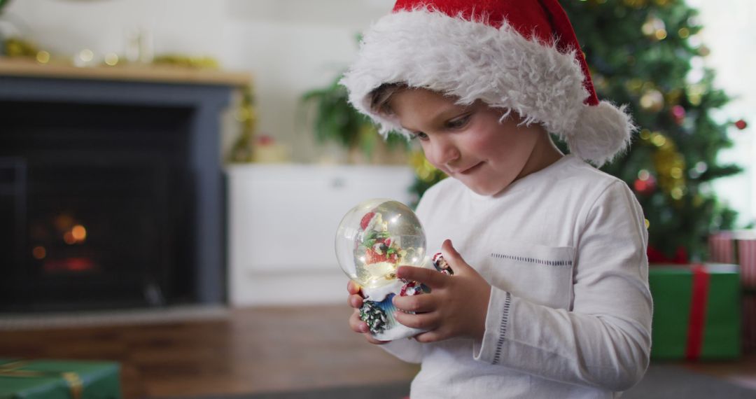 Cute Boy Holding Snow Globe Wearing Santa Hat During Christmas - Free Images, Stock Photos and Pictures on Pikwizard.com