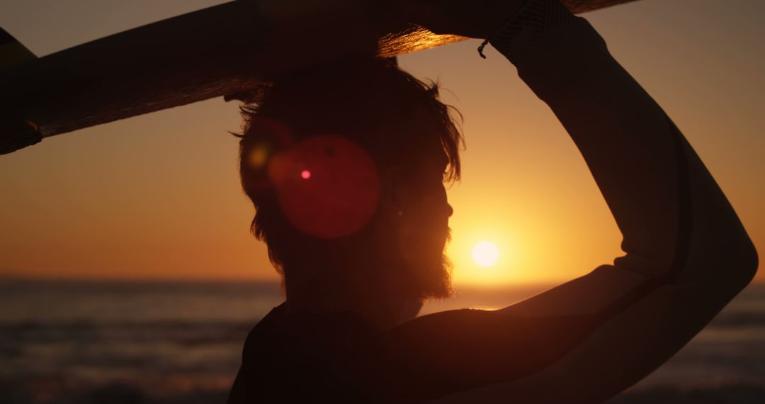 Silhouette of surfer at sunset with surfboard above head on beach - Free Images, Stock Photos and Pictures on Pikwizard.com