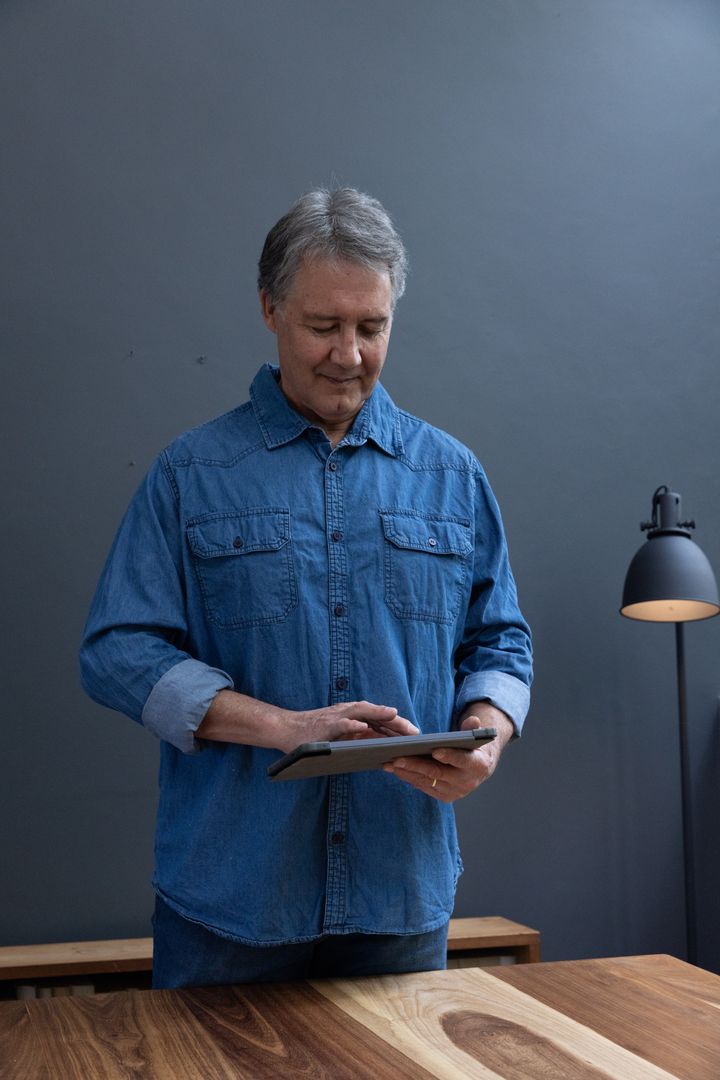 Senior Man Using Tablet in Modern Home Office with Wooden Desk