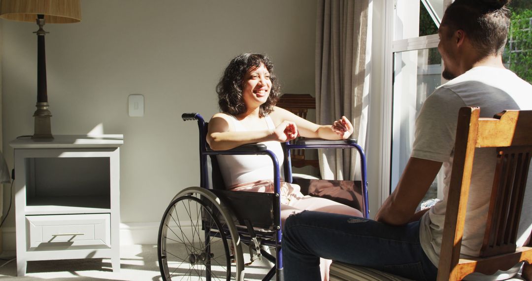 Biracial woman in wheelchair and male partner sitting and talking by window in sunny room - Free Images, Stock Photos and Pictures on Pikwizard.com