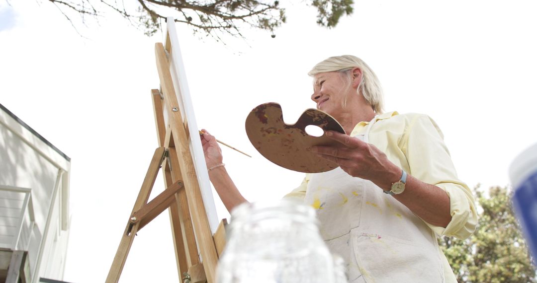 Older Woman Painting on Canvas Outdoors on Sunny Day - Free Images, Stock Photos and Pictures on Pikwizard.com