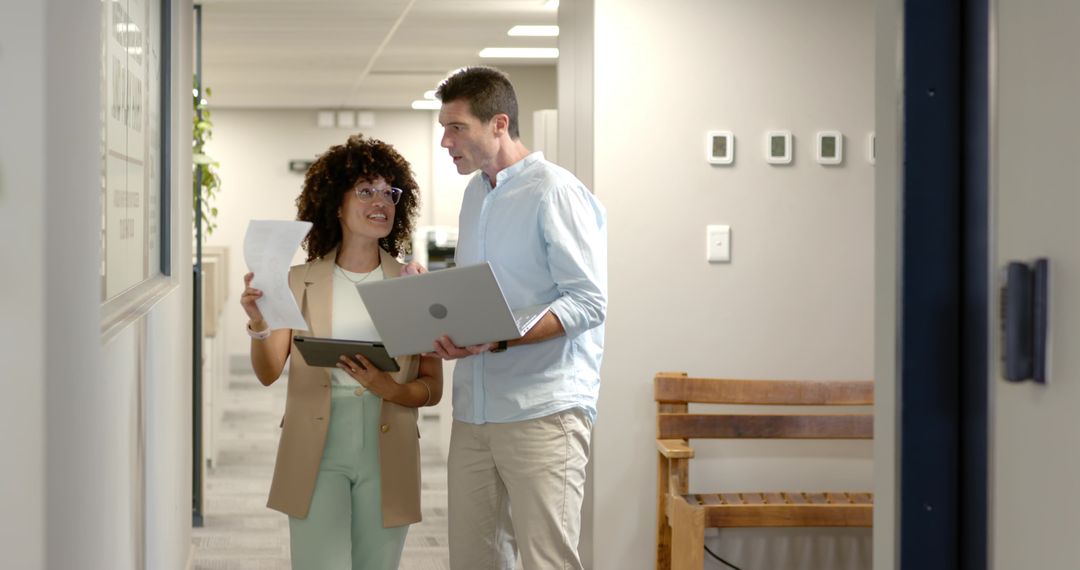 Coworkers Collaborating in Office Corridor with Laptop and Documents