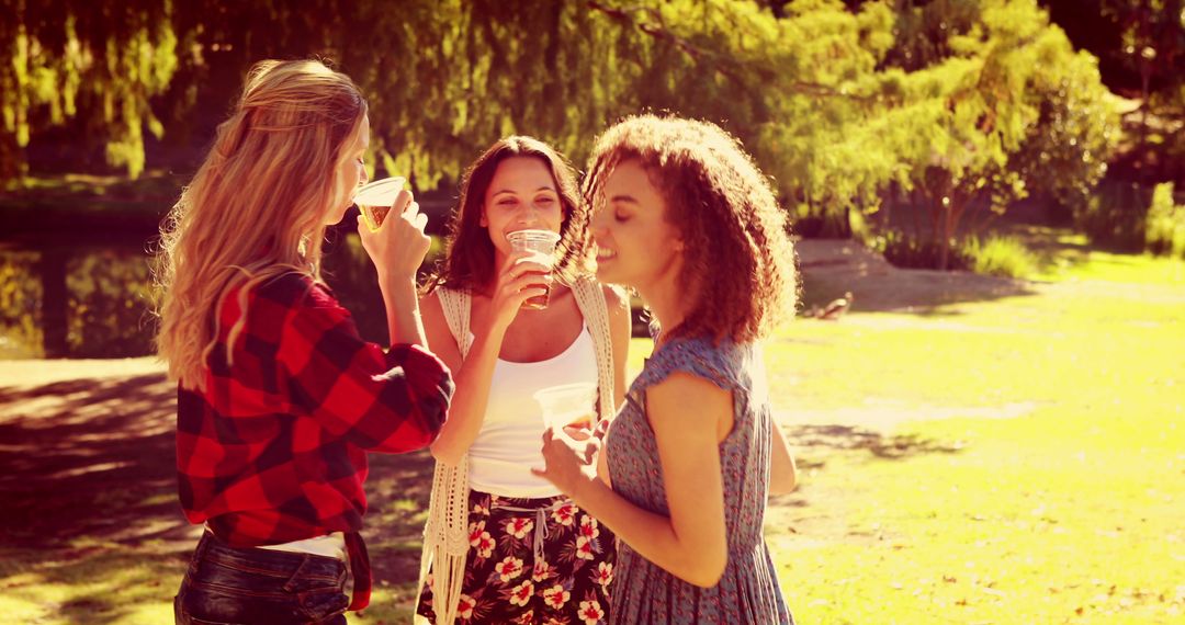 Young Women Enjoying Outdoor Picnic with Drinks in Sunlit Park - Free Images, Stock Photos and Pictures on Pikwizard.com