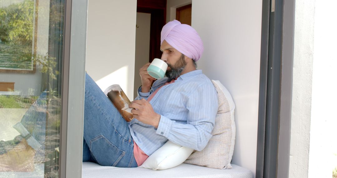 Man in Turban Relaxing at Home by Window with Book and Coffee
