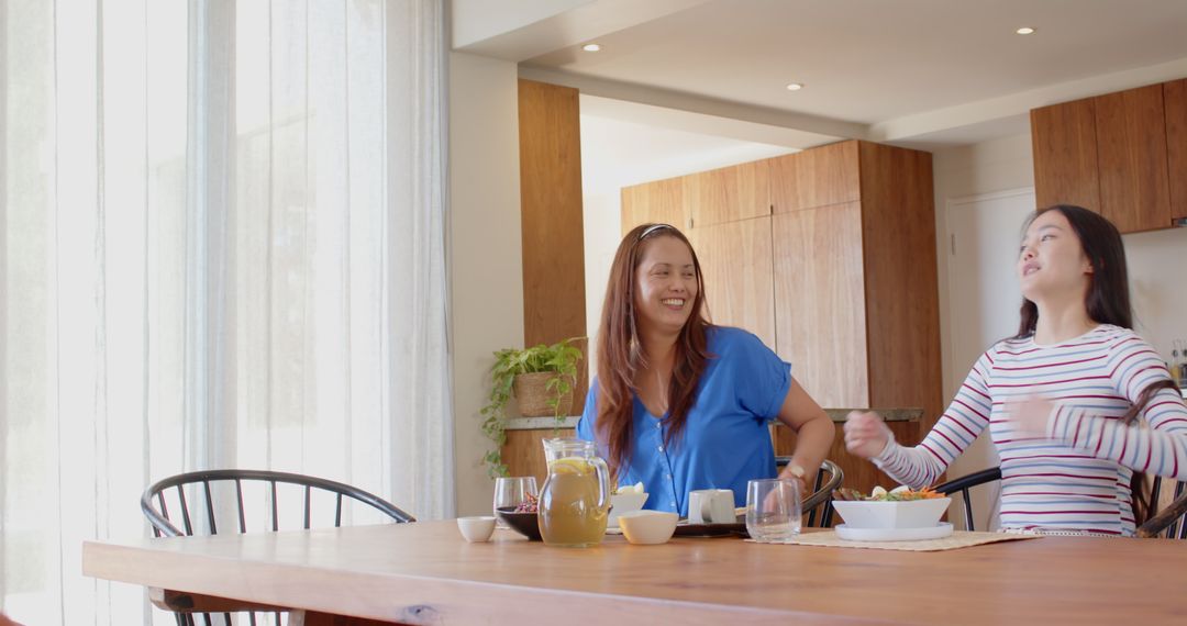 Mother and Daughter Relaxing at Home Dining Table with Salad and Juice